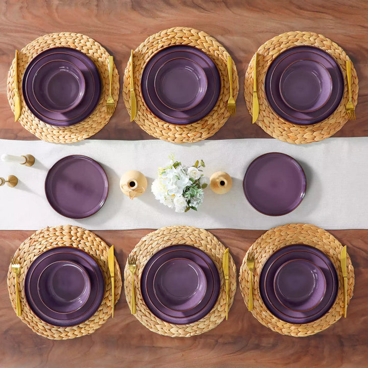 Sata purple stoneware 24-piece lipped edge dinnerware set flat lay empty plates woven placemat white linen table runner candlestick ceramic vase decor.