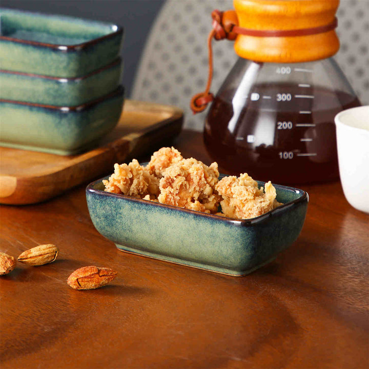 Green reactive-glaze rectangular dipping bowls with small bites, a coffee pot in the background, and scattered almonds for a natural table setting.