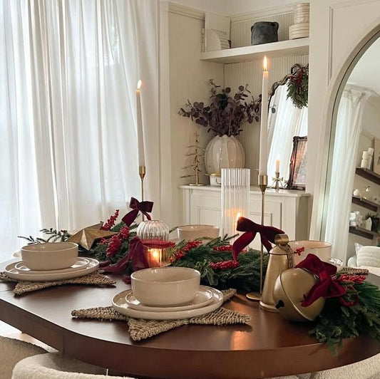 Plays 24-piece dinnerware set on a Christmas table with star-shaped woven placemats, golden candle holders, and pine branches tied with bows, creating a festive holiday ambiance.