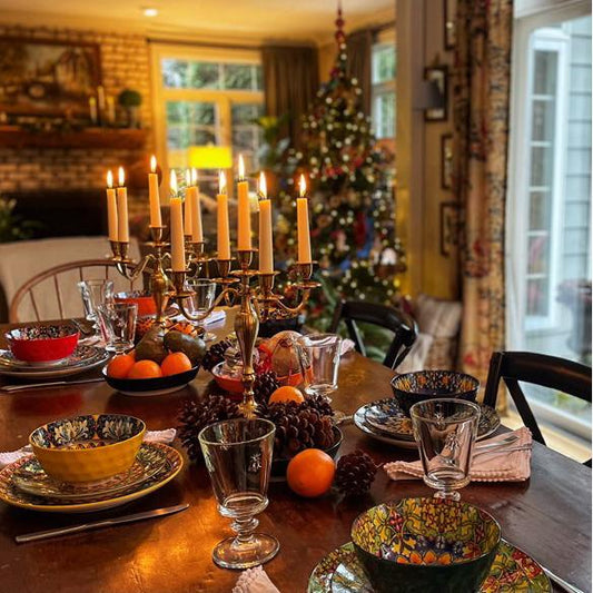 Cozy winter dining setup with Simi 24-Piece Dinnerware Set, featuring vibrant Bohemian porcelain, pinecones, and oranges, illuminated by soft candlelight.