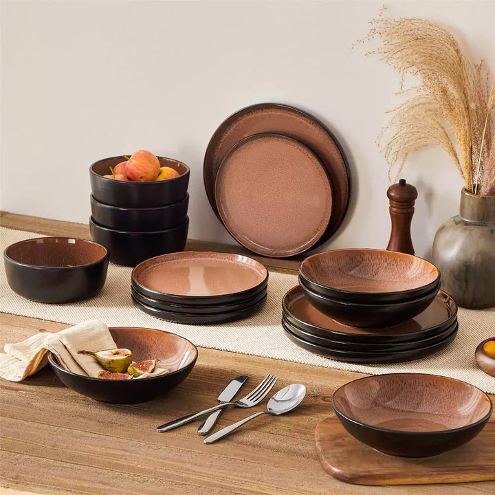 Amber red stoneware dinnerware set with a fig-topped soup plate on a brown wooden table and beige table runner.