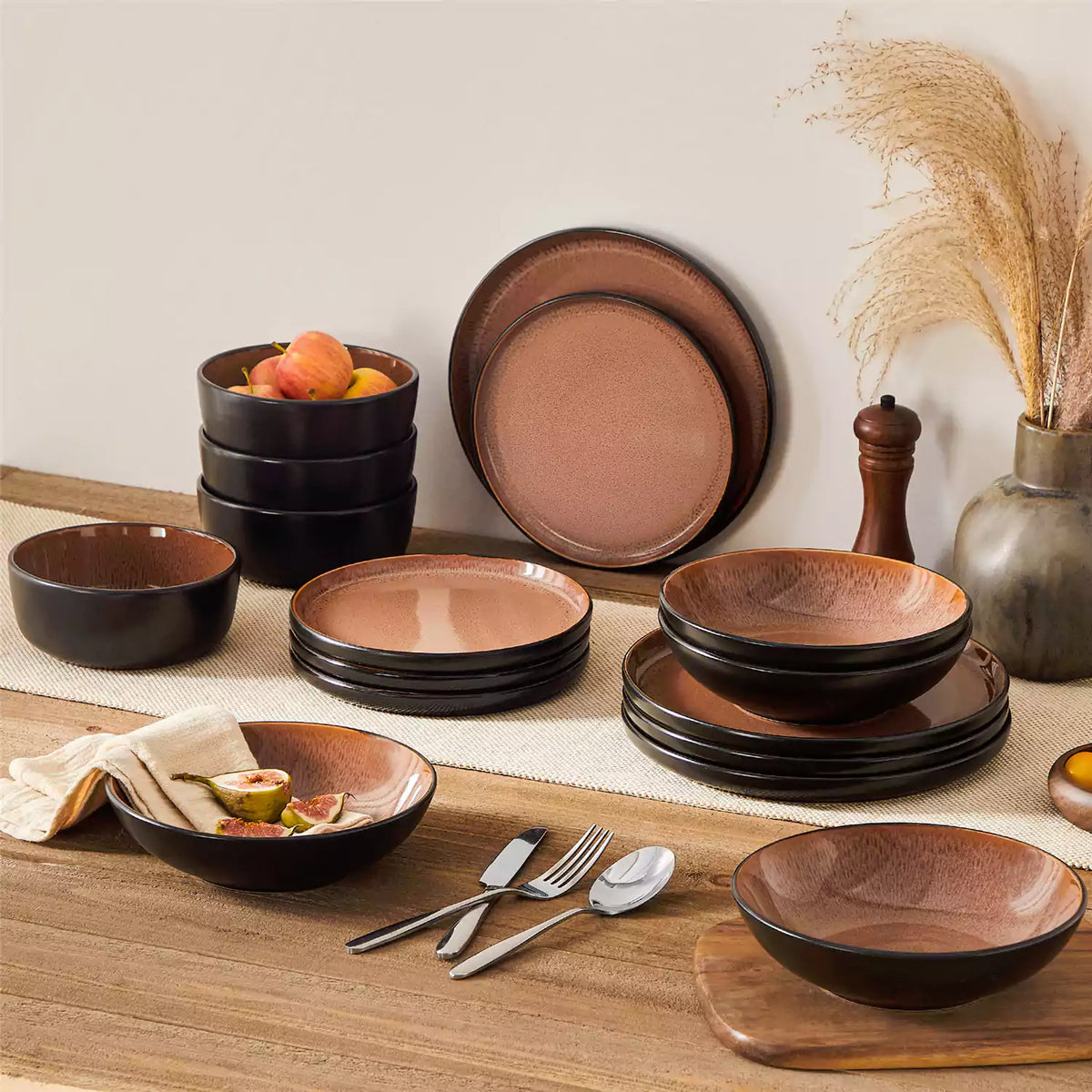 Rustic red stoneware dinnerware set styled on a wooden table with figs and apples, radiating cozy autumn charm.