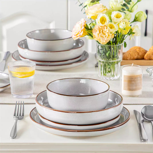 Stacked gray Loire stoneware dinnerware on a white table, styled with yellow roses, candles, and lemonade for a cozy, elegant table setting.
