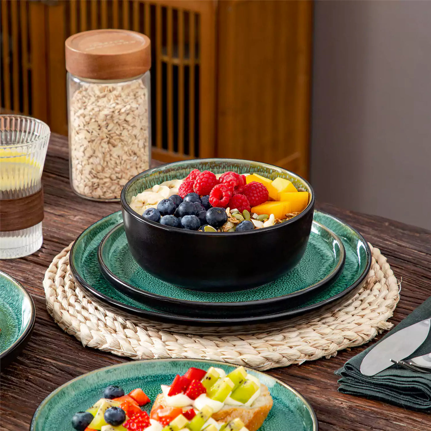 Green playa 18-piece stoneware dinnerware set with berry oat bowls stacked on plates, single dining set on woven mat