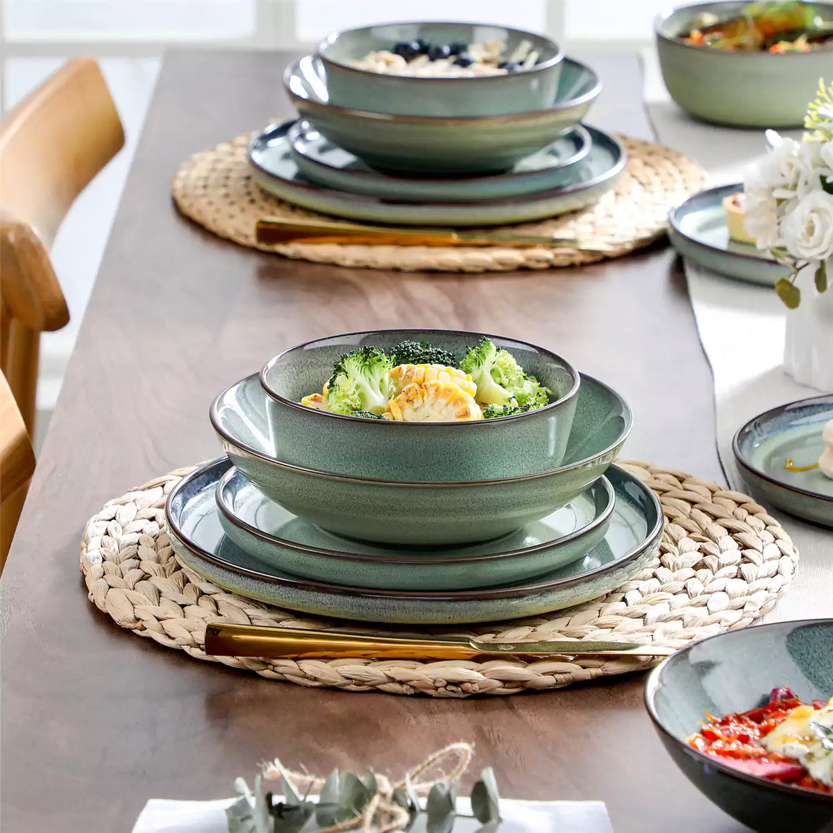 Sata green 24-piece dinnerware set with roasted cauliflower in stacked plates and bowls on rattan mat.