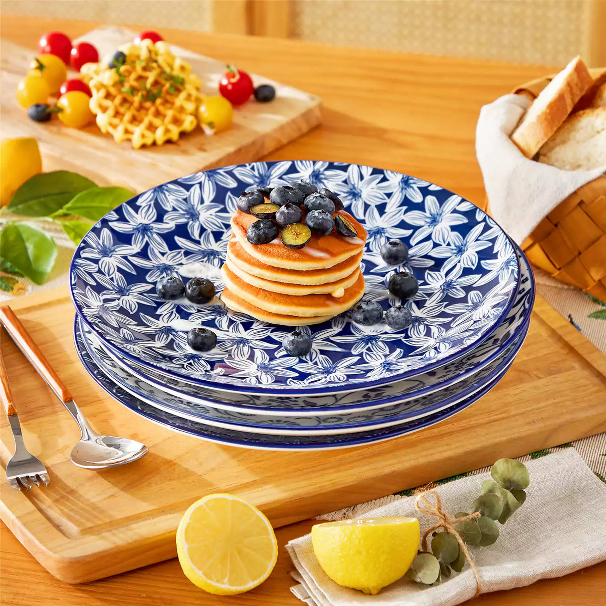 Stacked Selene porcelain dinner plates with fresh blueberries and waffles on a set table featuring lemons, cherry tomatoes, and a bread basket.