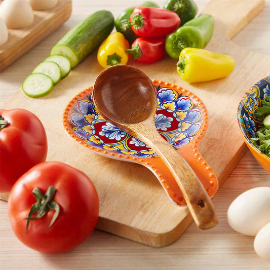 A sturdy ceramic spoon rest with a wooden spoon, surrounded by fresh tomatoes, cucumbers, and bell peppers.
