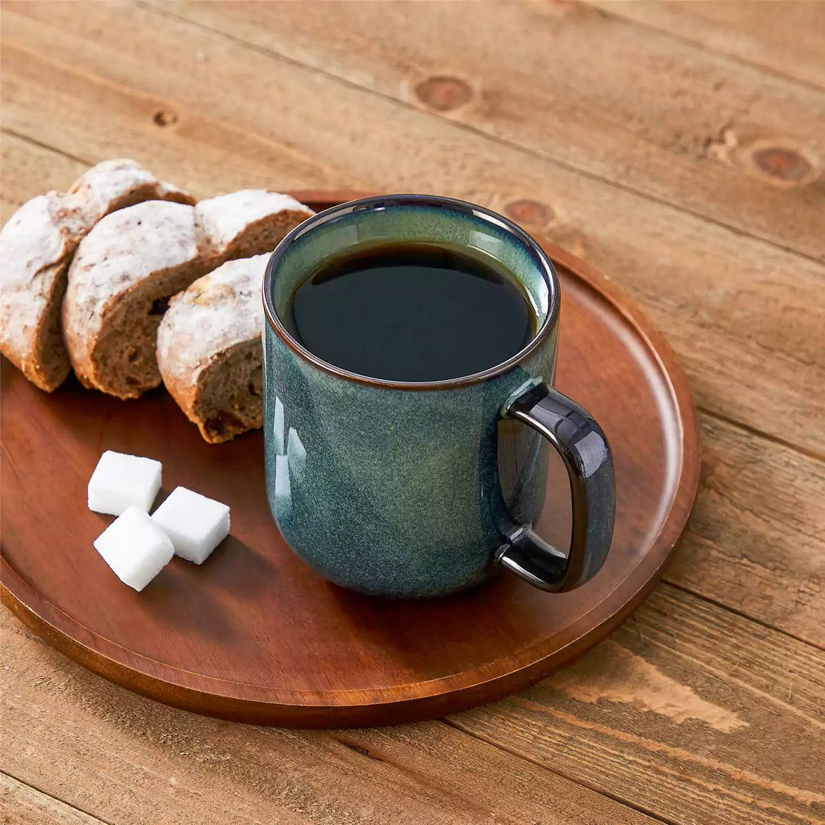 Starry green 16oz stoneware mugs with bread plates, sugar cubes, and pastries on a brown wooden table.