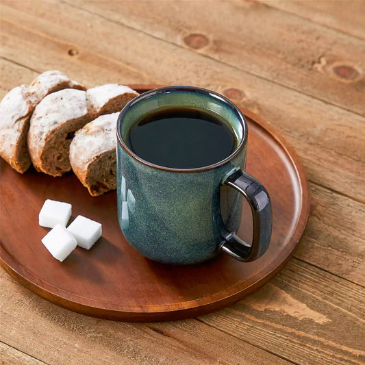 Starry green 16oz stoneware mugs with bread plates, sugar cubes, and pastries on a brown wooden table.