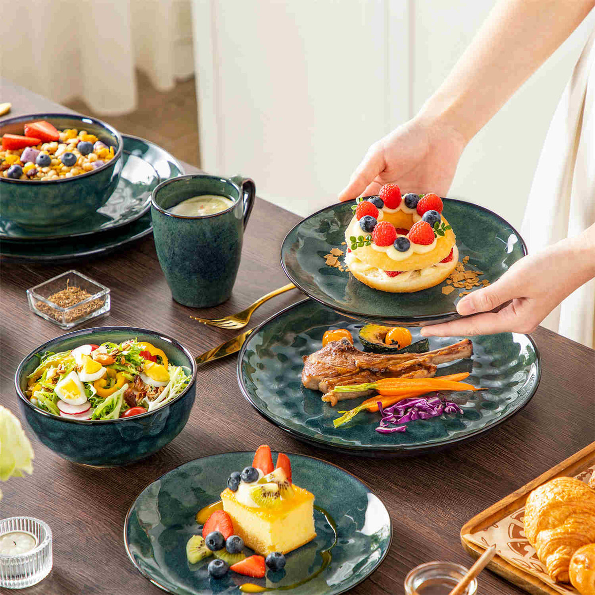 Green stoneware dinnerware set with teal tint on dark wooden table, model holding dessert plate with soufflé cupcake