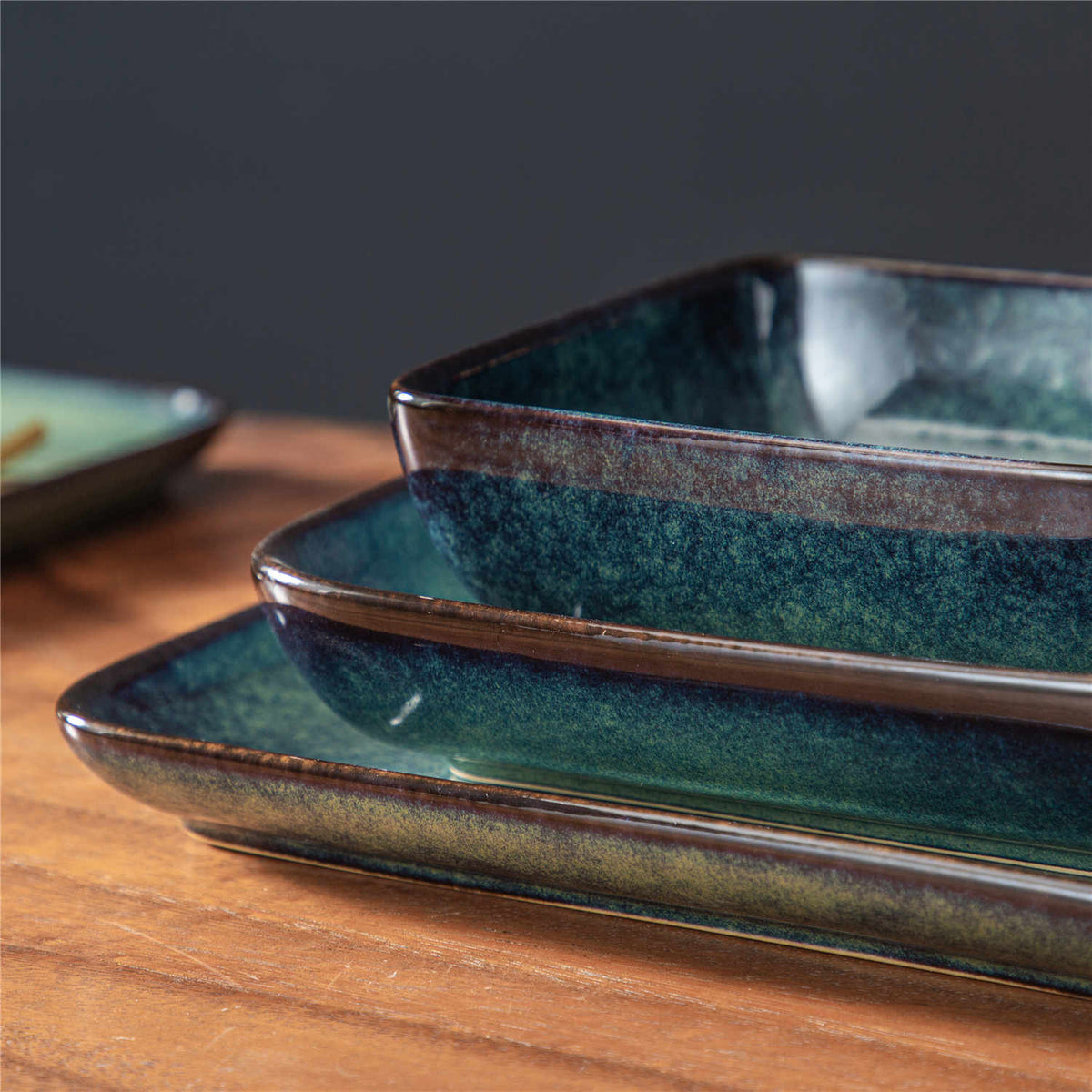 Stern green square stoneware plates stacked on a wood table, close-up view.