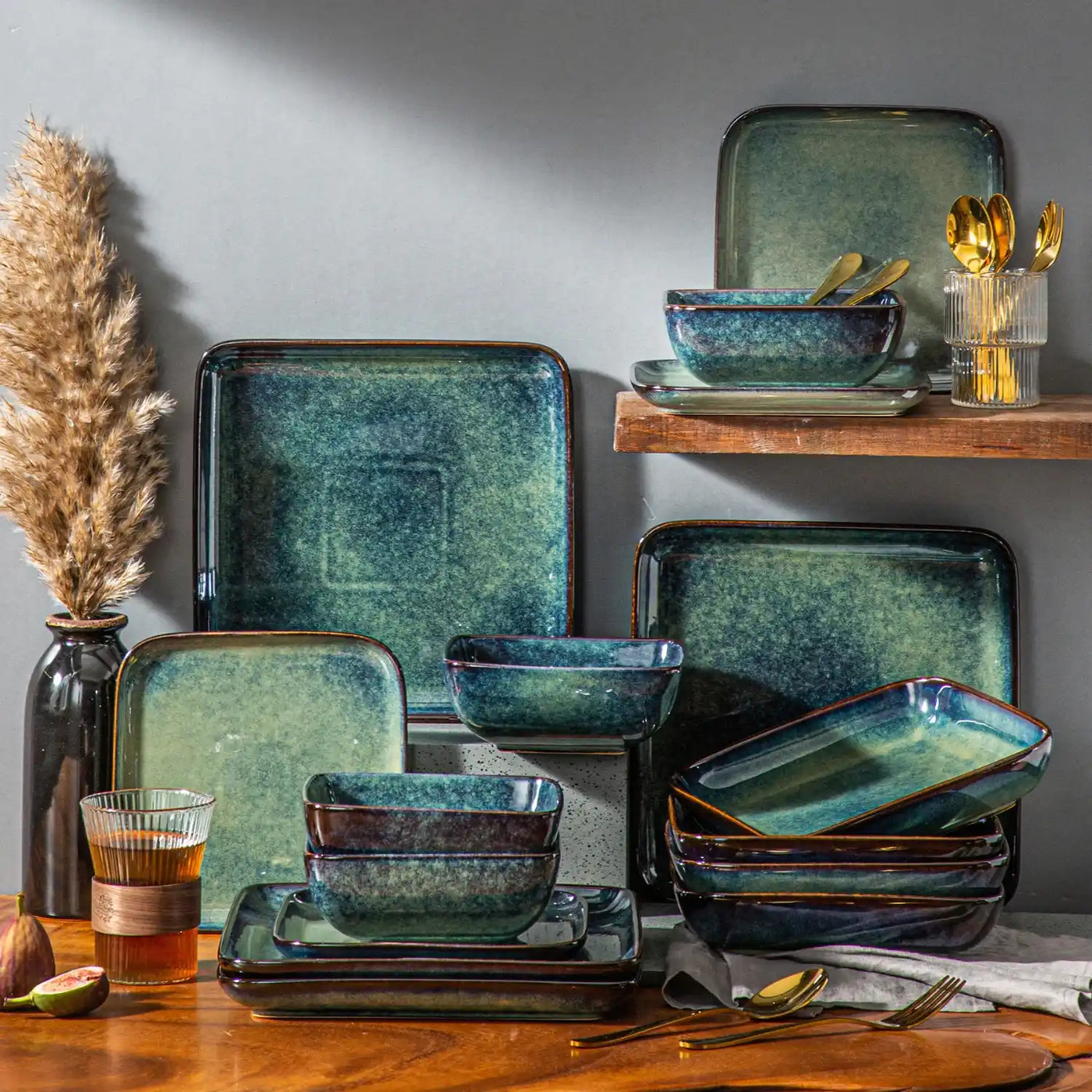 Green stoneware dinnerware stacked neatly on a wooden rack, adorned with figs and dry reeds, evoking a rustic, farmhouse charm.