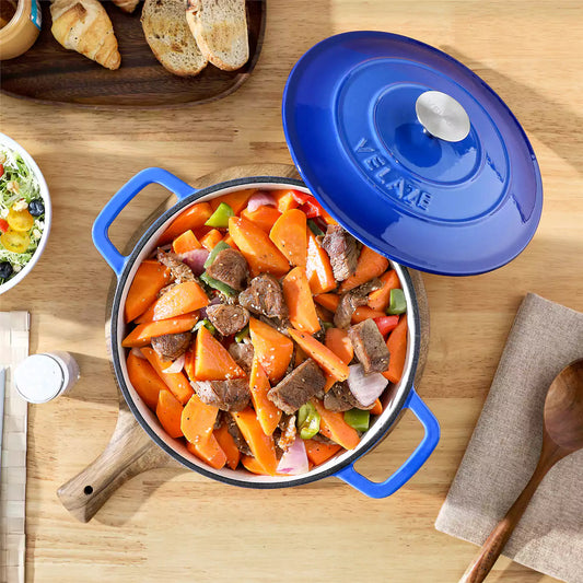 6qt blue enameled cast iron round Dutch oven with lid on beige wooden table, serving tender beef short ribs, accompanied by a salad bowl.