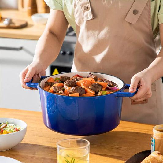 Blue 6QT Velaze enameled cast iron Dutch oven with hearty beef and carrot stew, held by model for serving