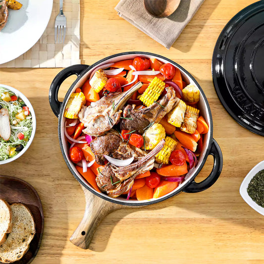 vancasso Black 6.5qt enameled cast iron dutch oven with roasted lamb chops, carrots and corn, served with fresh salad and bread cubes.