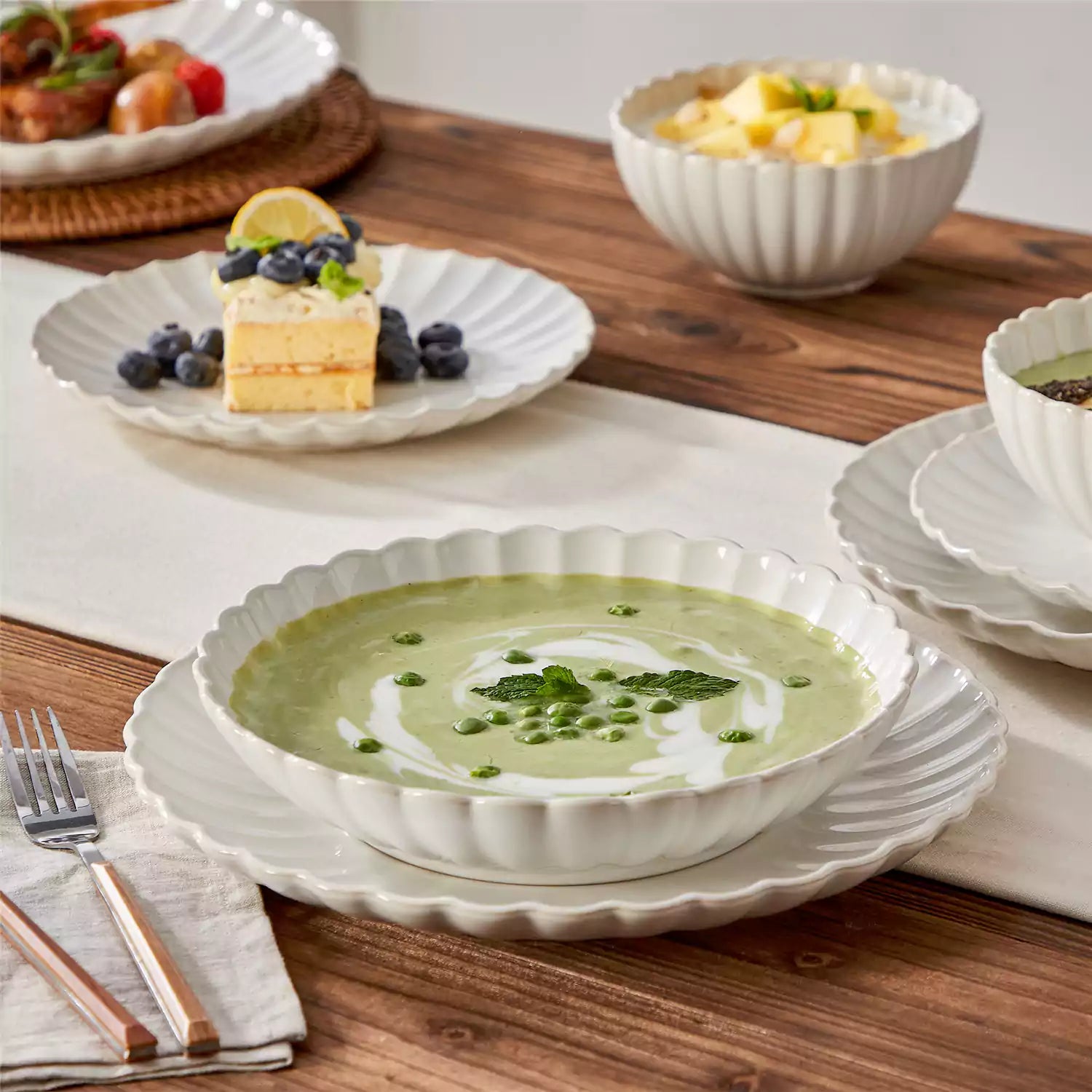 Adonis 16 piece reactive glaze dinnerware set in beige with pasta steak and fruit on a wooden dining table