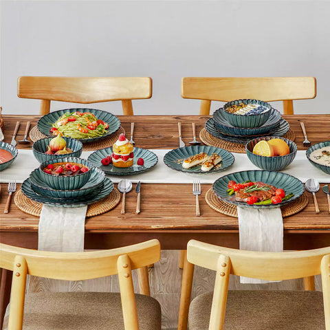 Adonis 16 piece reactive glaze dinnerware set in teal green with pasta steak and fruit on a wooden dining table