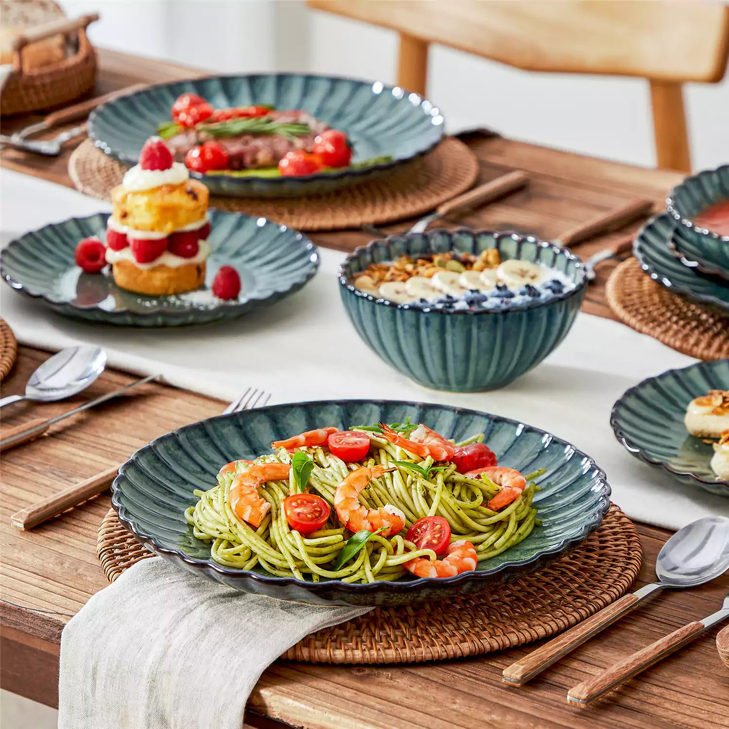 Adonis 16 piece reactive glaze dinnerware set in teal green with pasta steak and fruit on a wooden dining table