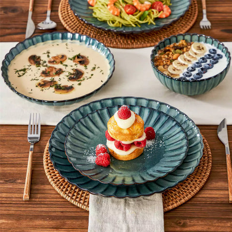 Adonis 16 piece reactive glaze dinnerware set in teal green with pasta steak and fruit on a wooden dining table