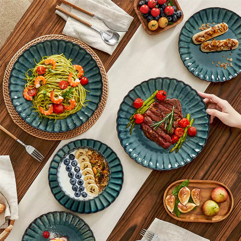Adonis 16 piece reactive glaze dinnerware set in teal green with pasta steak and fruit on a wooden dining table