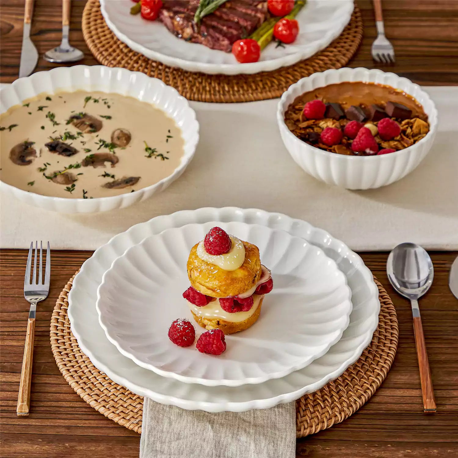 Adonis 16 piece white porcelain dinnerware set with steak pasta and fruit on a wooden dining table