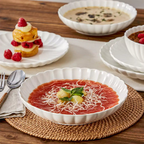 Adonis 16 piece white porcelain dinnerware set with steak pasta and fruit on a wooden dining table