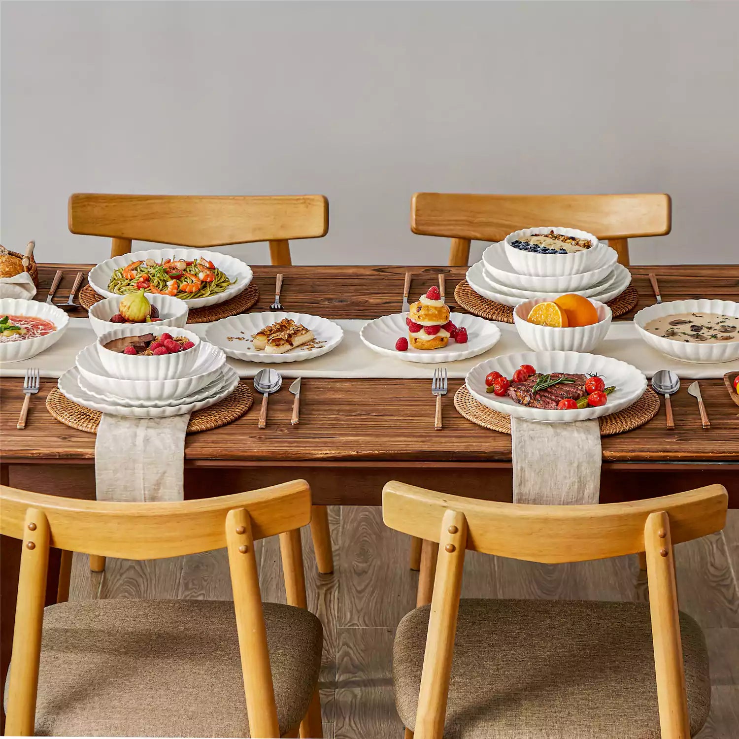 Adonis 16 piece white porcelain dinnerware set with steak pasta and fruit on a wooden dining table
