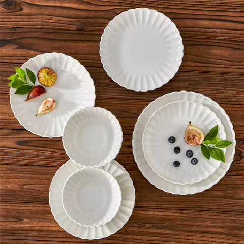 Adonis 16 piece white porcelain dinnerware set with steak pasta and fruit on a wooden dining table