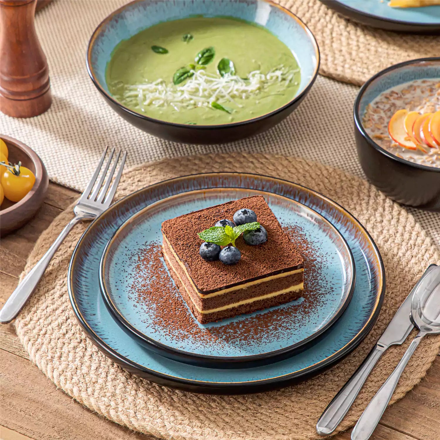 Assorted dishes with soup - dessert - and fruit salad on rustic wooden table - Amber 16-Piece blue stoneware dinnerware set with plates and bowls by vancasso