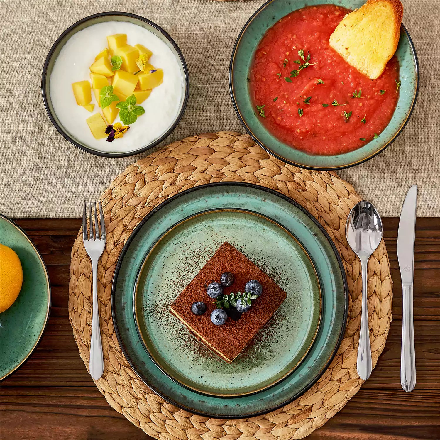 Assorted dishes with soup - dessert - and fruit salad on rustic wooden table - Amber 16-Piece green stoneware dinnerware set with plates and bowls by vancasso
