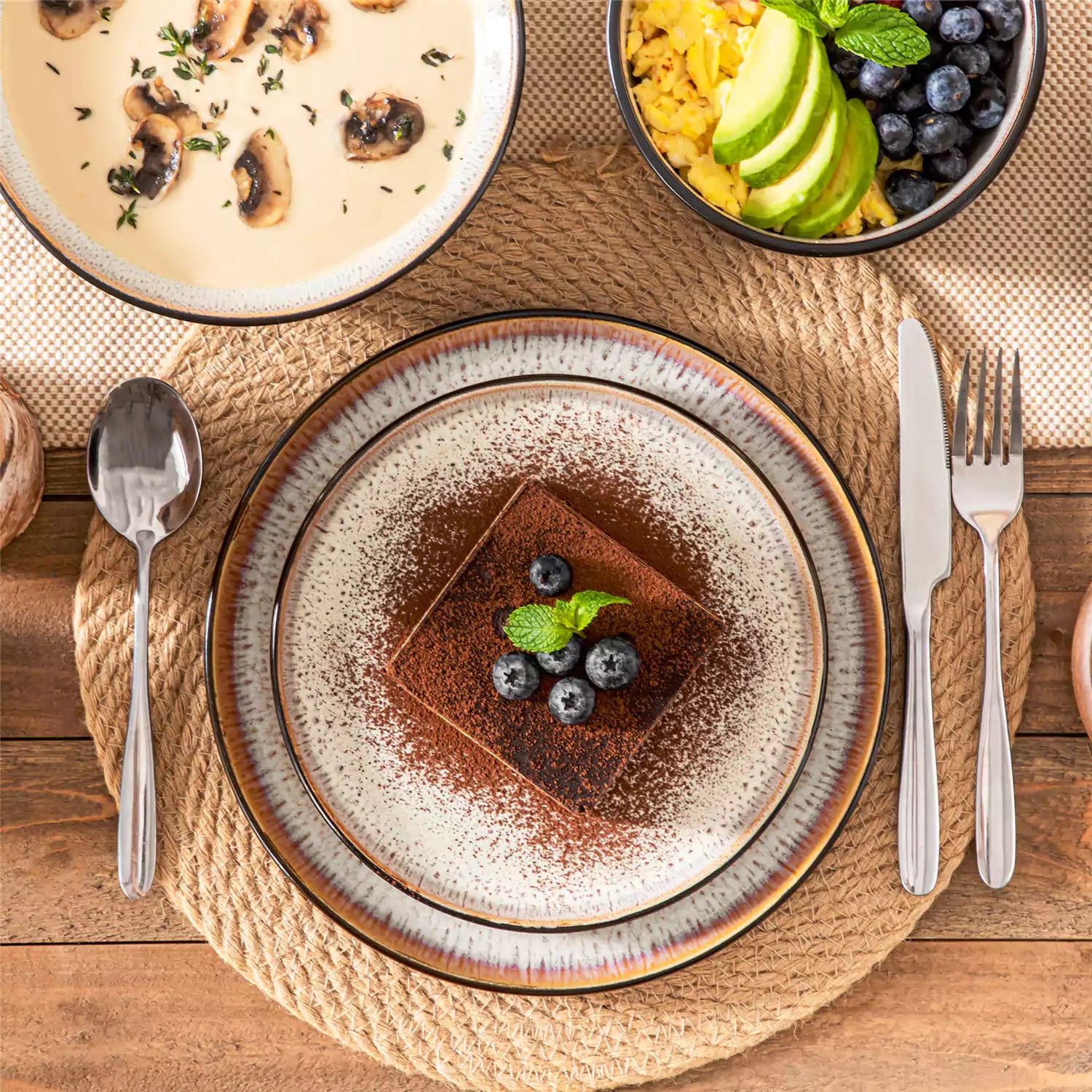 Assorted dishes with soup - dessert - and fruit salad on rustic wooden table - Amber 16-Piece beige stoneware dinnerware set with plates and bowls by vancasso
