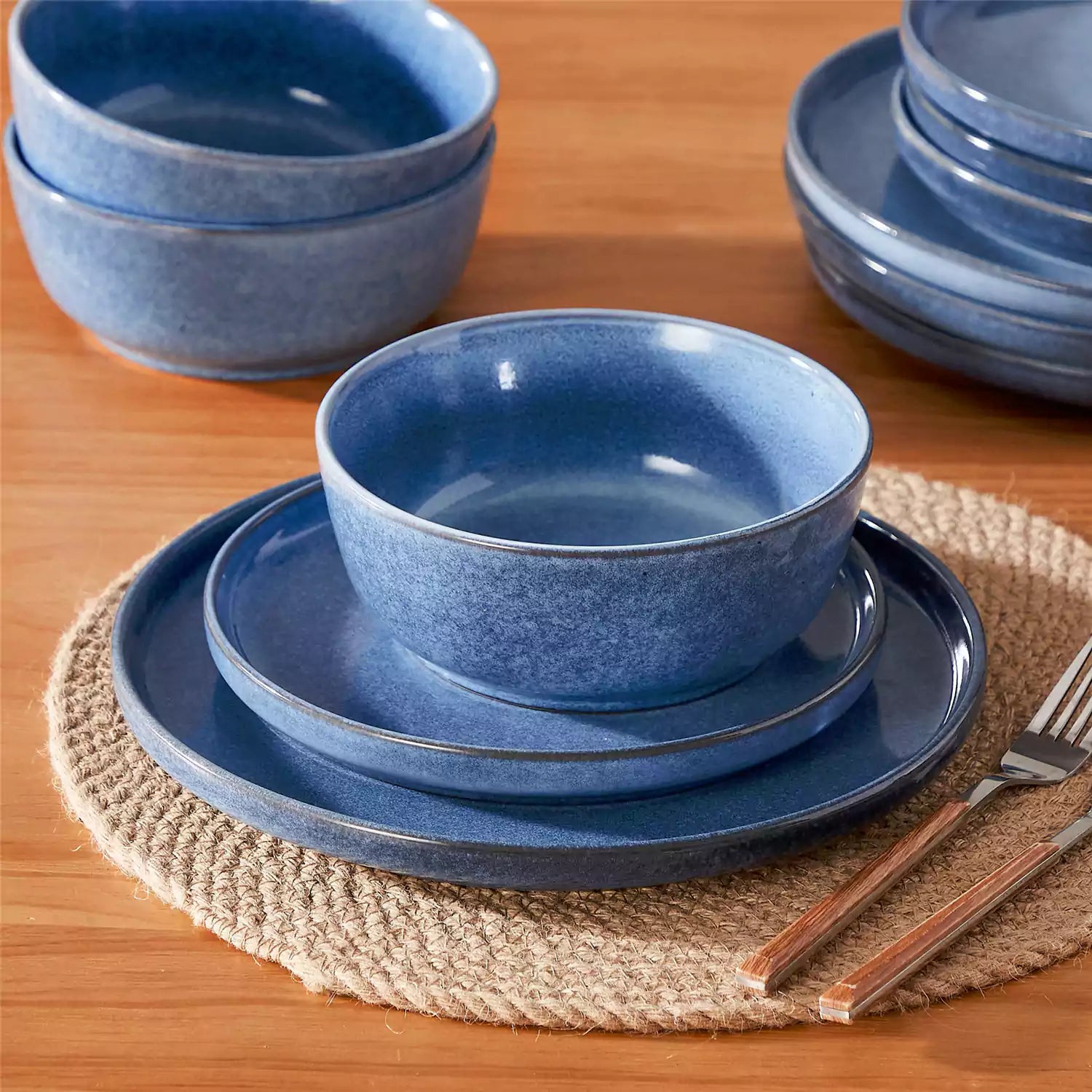 Blue stoneware plates and bowls with reactive glaze on farmhouse wooden table with woven placemats
