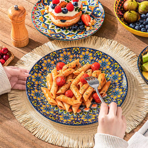 Lumi 24 piece porcelain dinnerware set with vibrant patterns stacked on a wooden table with colorful placemats and assorted dishes