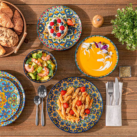 Lumi 24 piece porcelain dinnerware set with vibrant patterns stacked on a wooden table with colorful placemats and assorted dishes