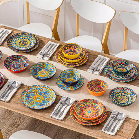 Lumi 24 piece porcelain dinnerware set with vibrant patterns stacked on a wooden table with colorful placemats and assorted dishes