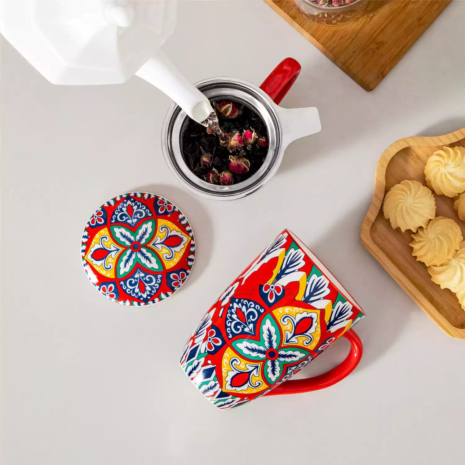Lumi flame red porcelain tea mug with infuser and lid featuring vibrant Bohemian pattern on a wooden desk with laptop and plant