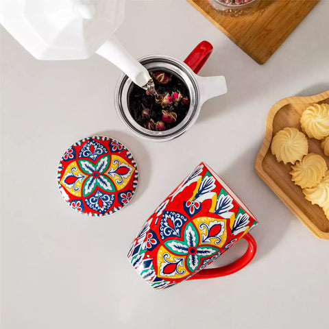 Lumi flame red porcelain tea mug with infuser and lid featuring vibrant Bohemian pattern on a wooden desk with laptop and plant