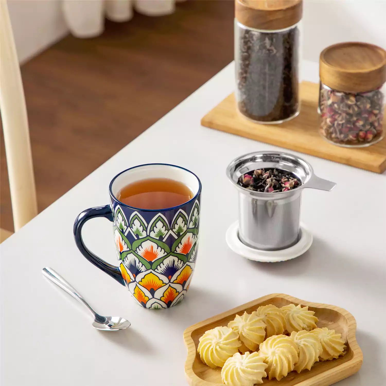 Lumi hunter green porcelain tea mug with infuser and lid featuring vibrant Bohemian pattern on a wooden desk with laptop and plant