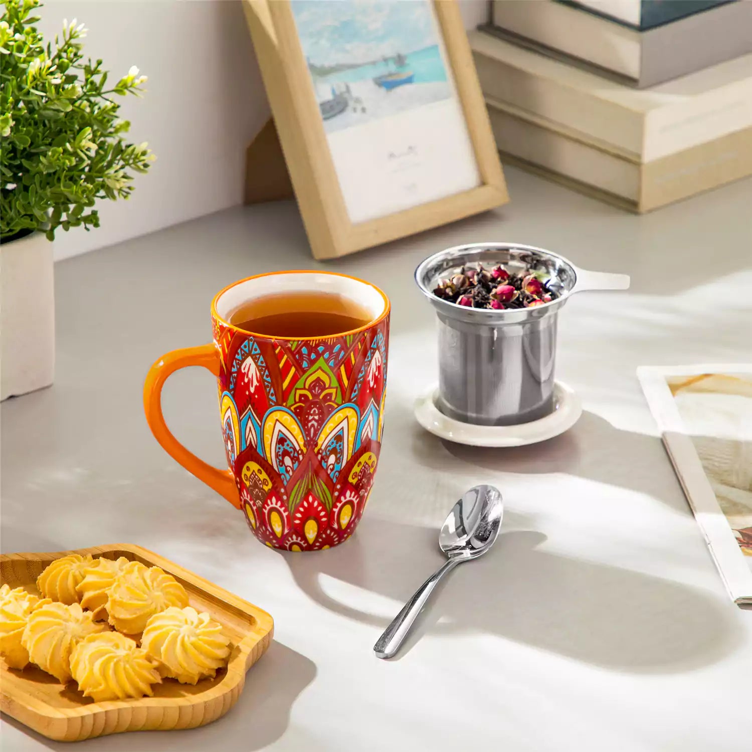 Lumi bold orange porcelain tea mug with infuser and lid featuring vibrant Bohemian pattern on a wooden desk with laptop and plant
