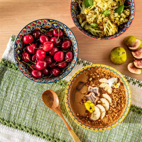 Colorful 26oz Lumi porcelain bowls on rattan placemats filled with oatmeal berries roasted broccoli and cherries on a linen table runner