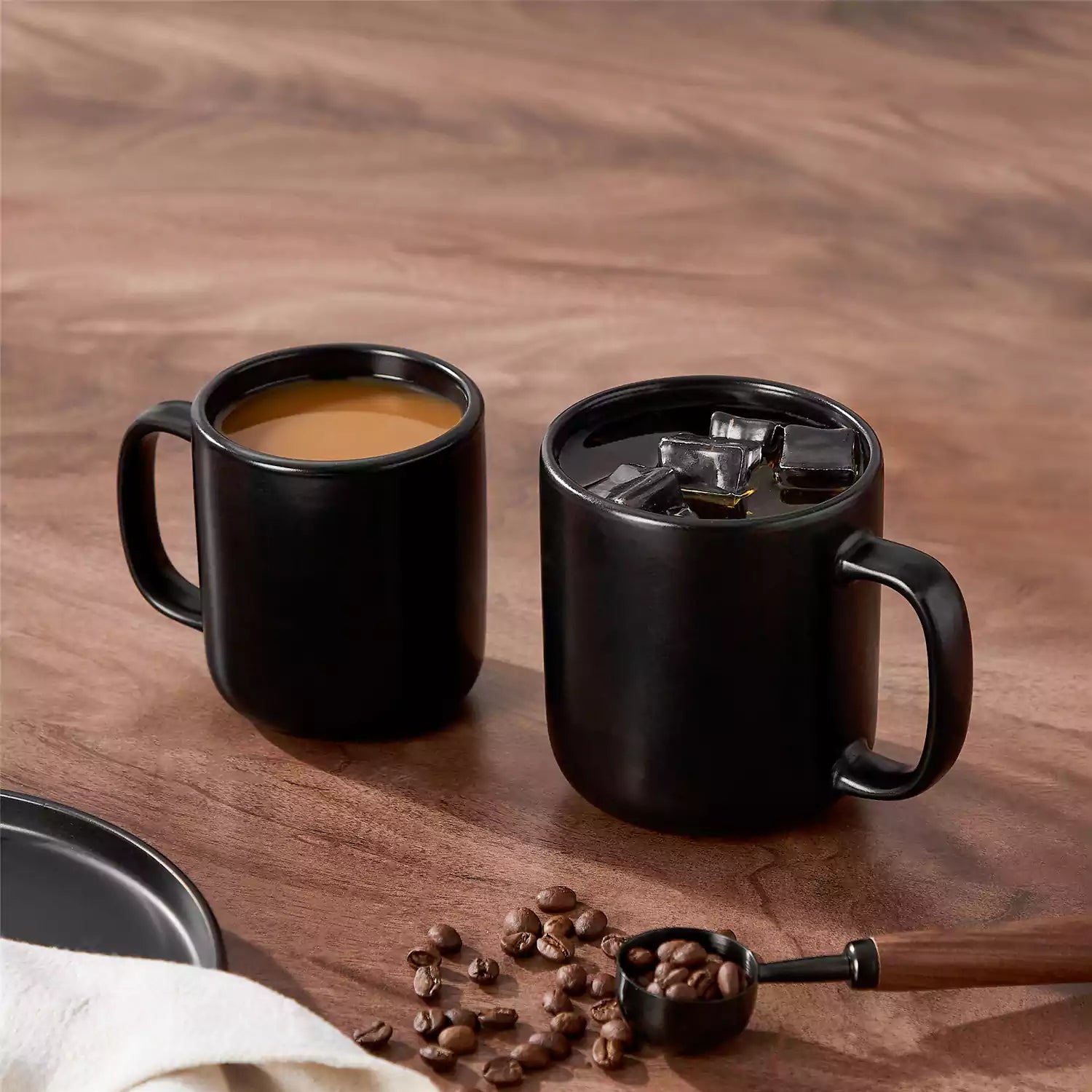 Playa 16oz stoneware mugs in black reactive glaze on a rustic wooden café table with coffee maker and pastries