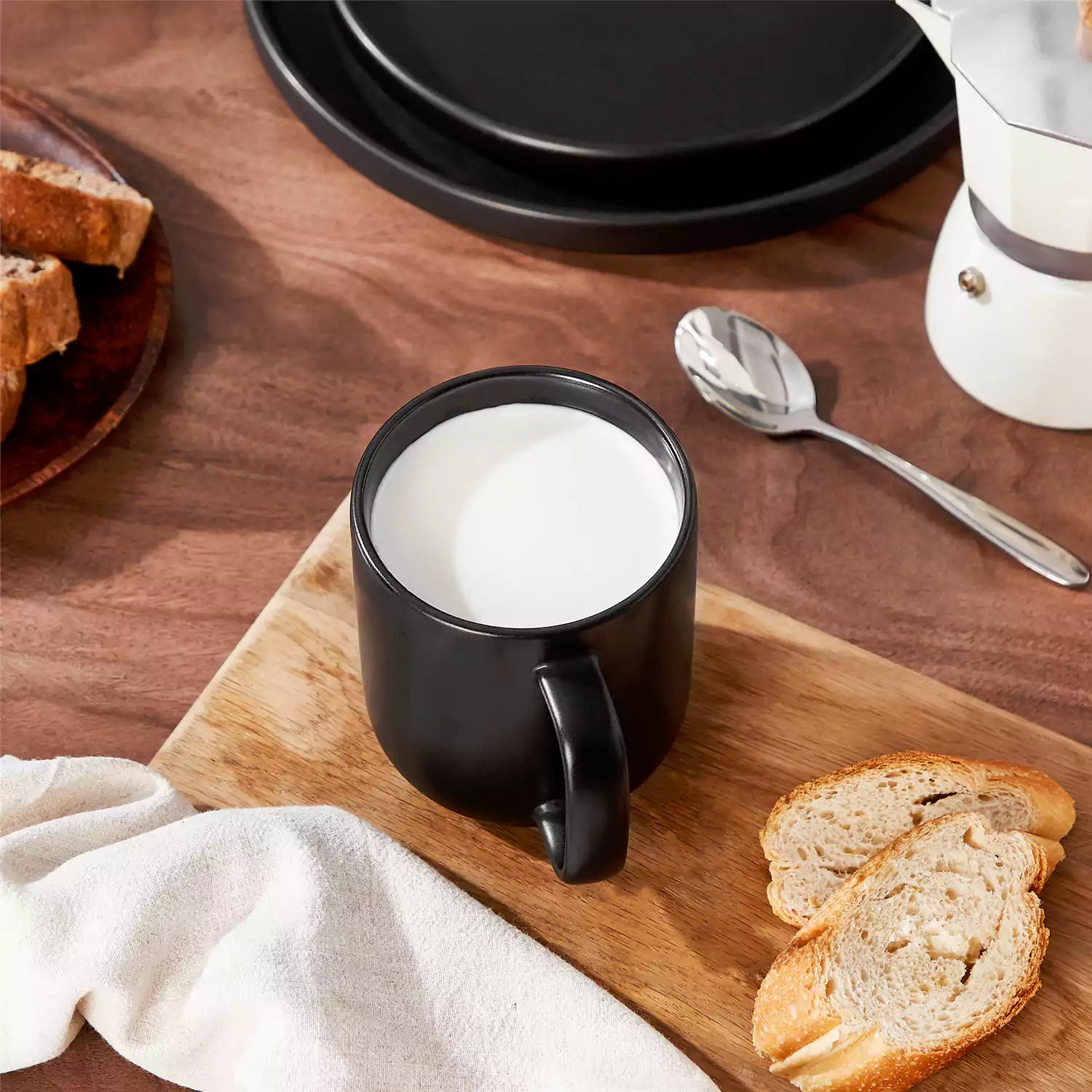 Playa 16oz stoneware mugs in black reactive glaze on a rustic wooden café table with coffee maker and pastries