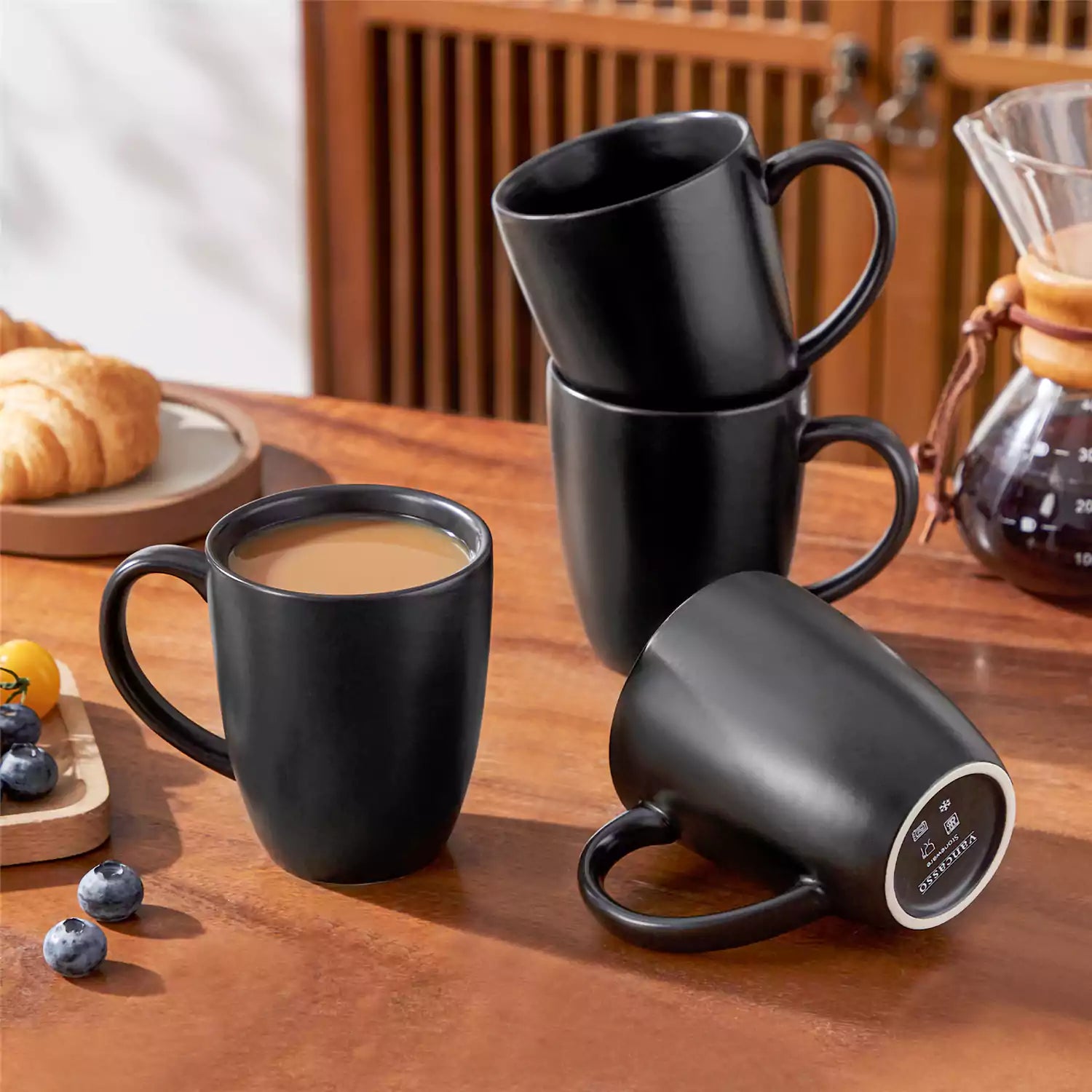 Playa set of four black stoneware mugs and a classic Moka pot on a wooden tray with a morning brew beside fresh pastries and coffee beans