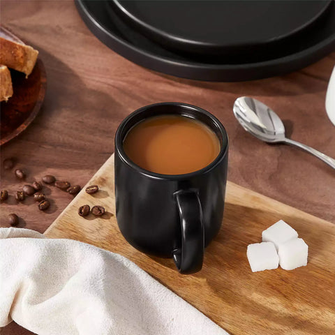Playa 12oz stoneware mug in solid matte black on a rustic wooden surface for a moody coffee break with spoon and scattered beans