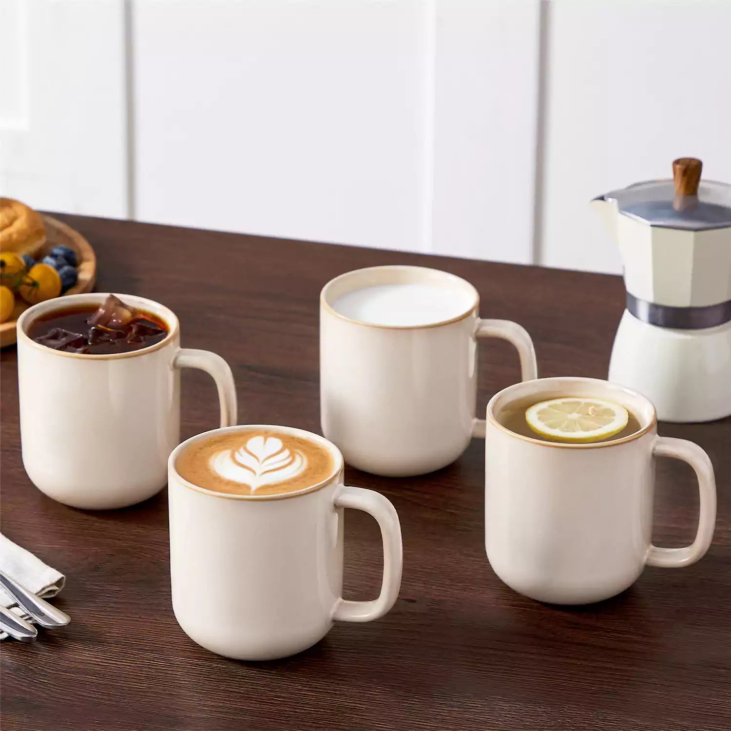Playa 16oz stoneware mugs in beige reactive glaze on a rustic wooden café table with coffee maker and pastries