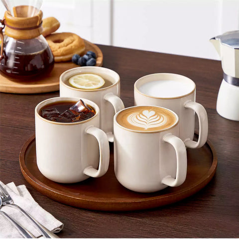 Playa 16oz stoneware mugs in beige reactive glaze on a rustic wooden café table with coffee maker and pastries