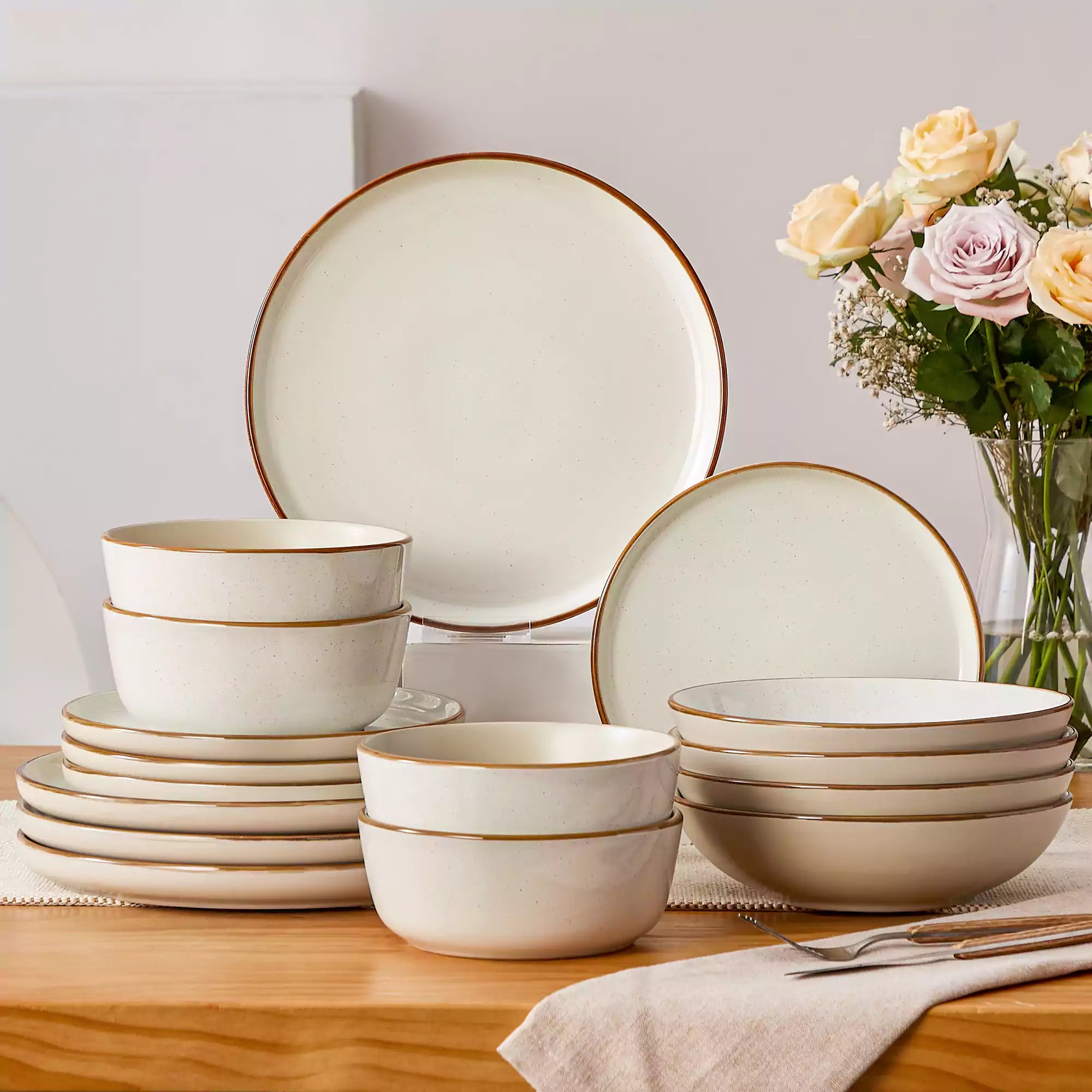 Rustic beige speckled stoneware dinnerware set with lipped-edge plates and bowls arranged on a sunlit modern dining table-vancasso