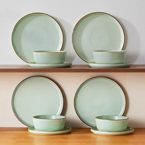Green rustic stoneware dinnerware set with speckled - lipped-edge plates and bowls on a dining table with flowers and cutlery in a cozy modern kitchen-vancasso