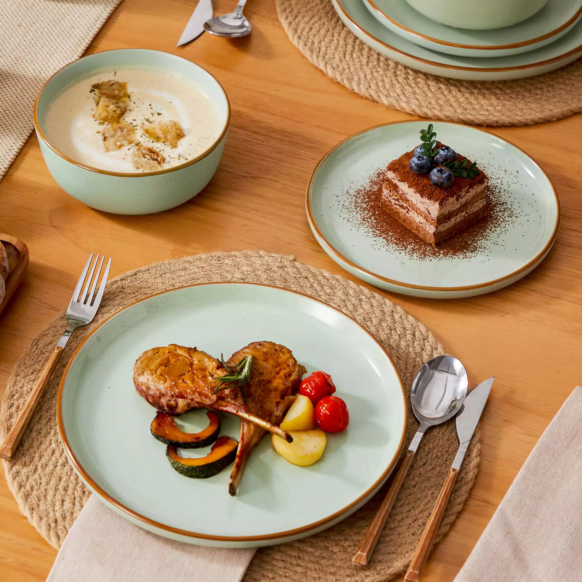 Green rustic stoneware dinnerware set with speckled - lipped-edge plates and bowls on a dining table with flowers and cutlery in a cozy modern kitchen-vancasso