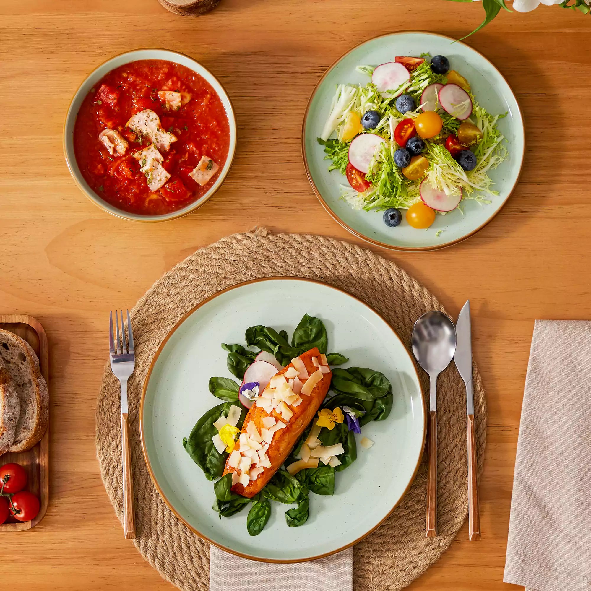 Green rustic stoneware dinnerware set with speckled - lipped-edge plates and bowls on a dining table with flowers and cutlery in a cozy modern kitchen-vancasso